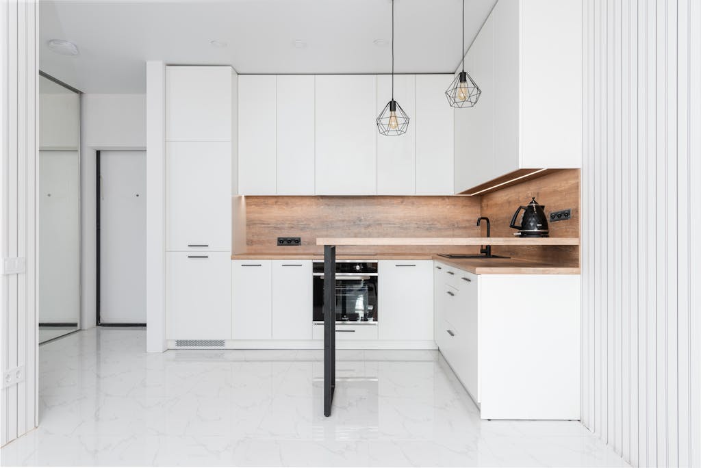 Contemporary spacious convenient kitchen with modern white interior and geometrical metal lamps in daytime