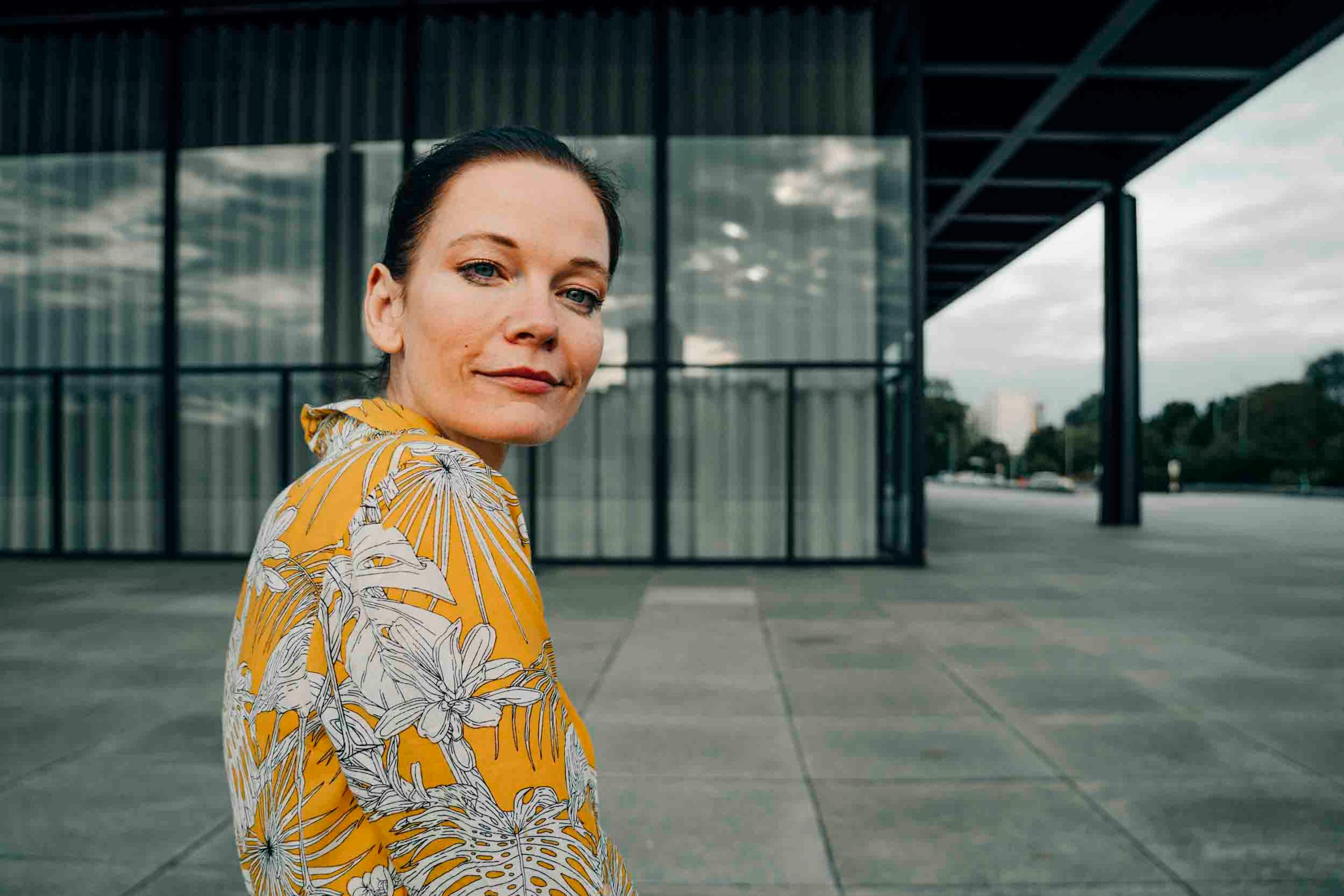 Elegant portrait of a woman in a yellow floral dress against modern Berlin architecture.